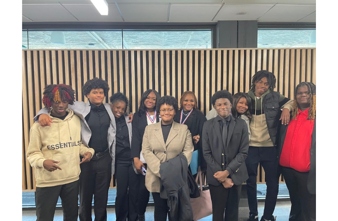  A group of well-dressed high school students and their teacher pose proudly together indoors 